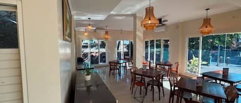 Un amplio comedor con varias mesas y sillas, ventanas grandes que ofrecen vistas al exterior, e iluminación colgante.