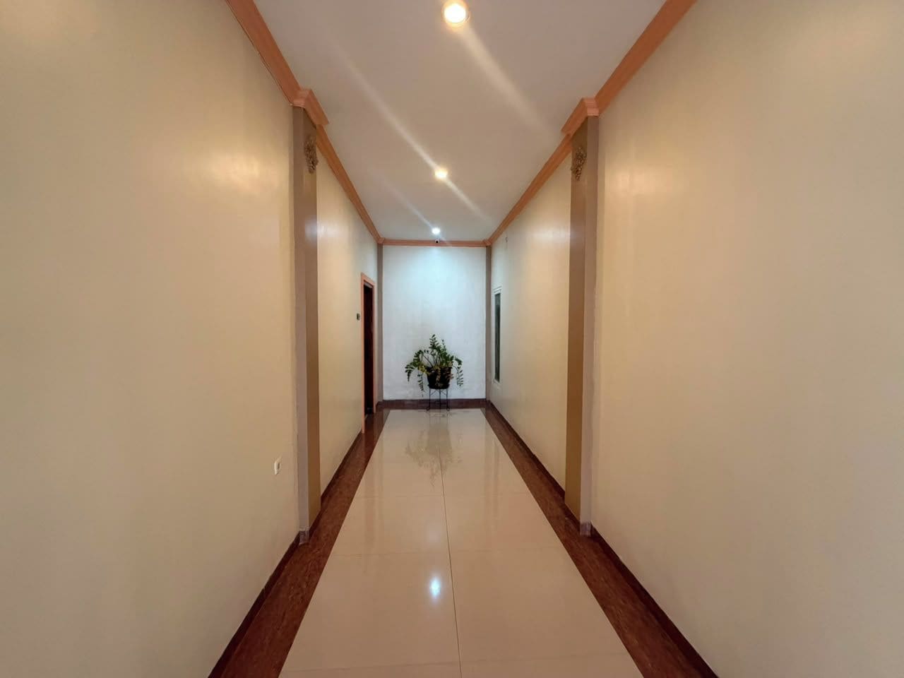 A long, narrow hallway with a polished floor, flanked by plain walls and wooden trim.