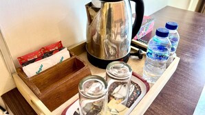 A tray with a kettle, sugar packets, water bottles, and glasses. - Famora Stay Kuta Bali (Kuta)