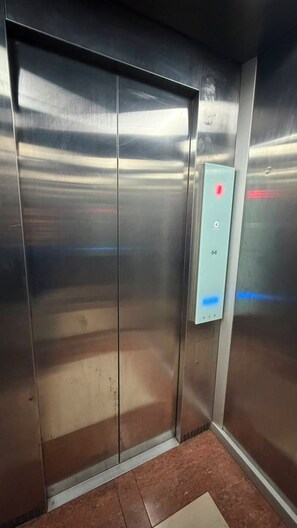 A metallic elevator with a control panel featuring buttons and a red light indicator. - Famora Stay Kuta Bali (Kuta)