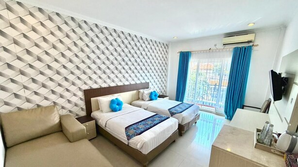 A hotel room with a patterned wall, two beds with blue pillows, a sofa, a desk, and a TV. - Famora Stay Kuta Bali (Kuta)