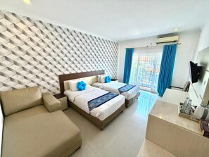 A hotel room with a patterned wall, two beds with blue pillows, a sofa, a desk, and a TV. - Famora Stay Kuta Bali (Kuta)