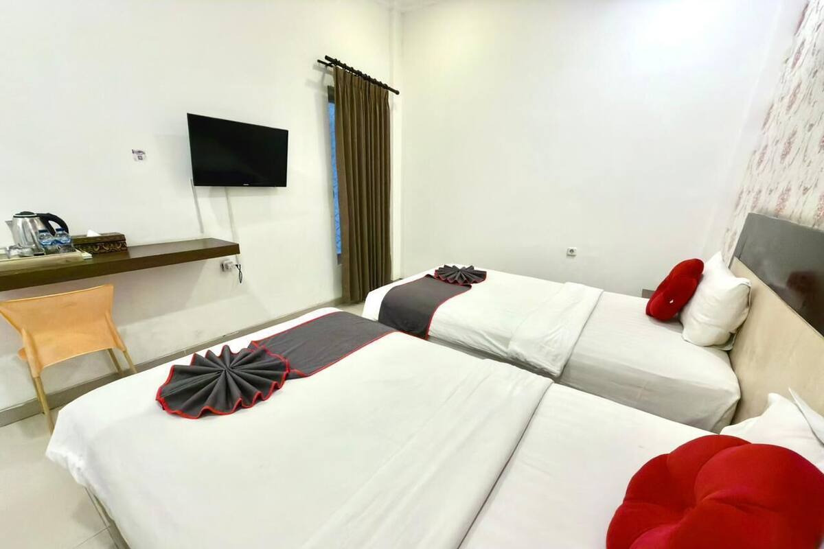 A hotel room with two beds, a desk, a television, and a window with curtains.