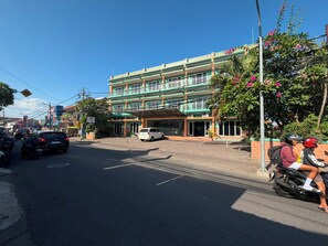 A multi-story building with a green facade, parked cars, and a motorcycle with two riders. - Famora Stay Kuta Bali (Kuta)