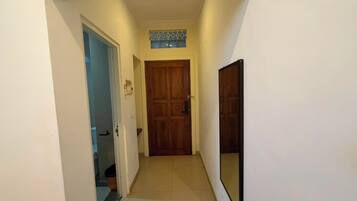 A narrow hallway with a wooden door at the end, a tiled floor, and a wall-mounted mirror.