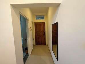 A narrow hallway with a wooden door at the end, a tiled floor, and a wall-mounted mirror. - Famora Stay Kuta Bali (Kuta)