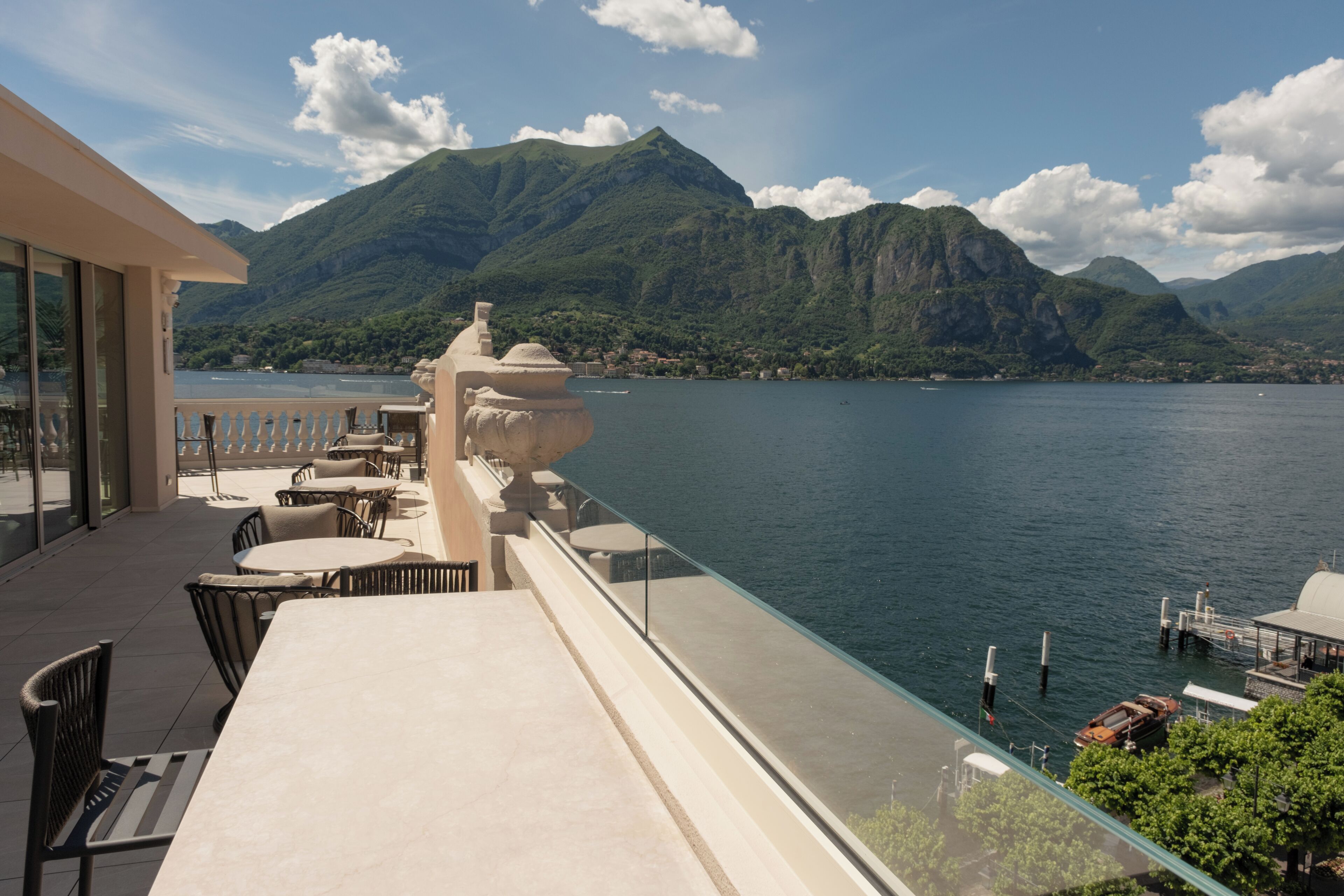 Terraza con mesas al aire libre, vista a un lago y montañas.