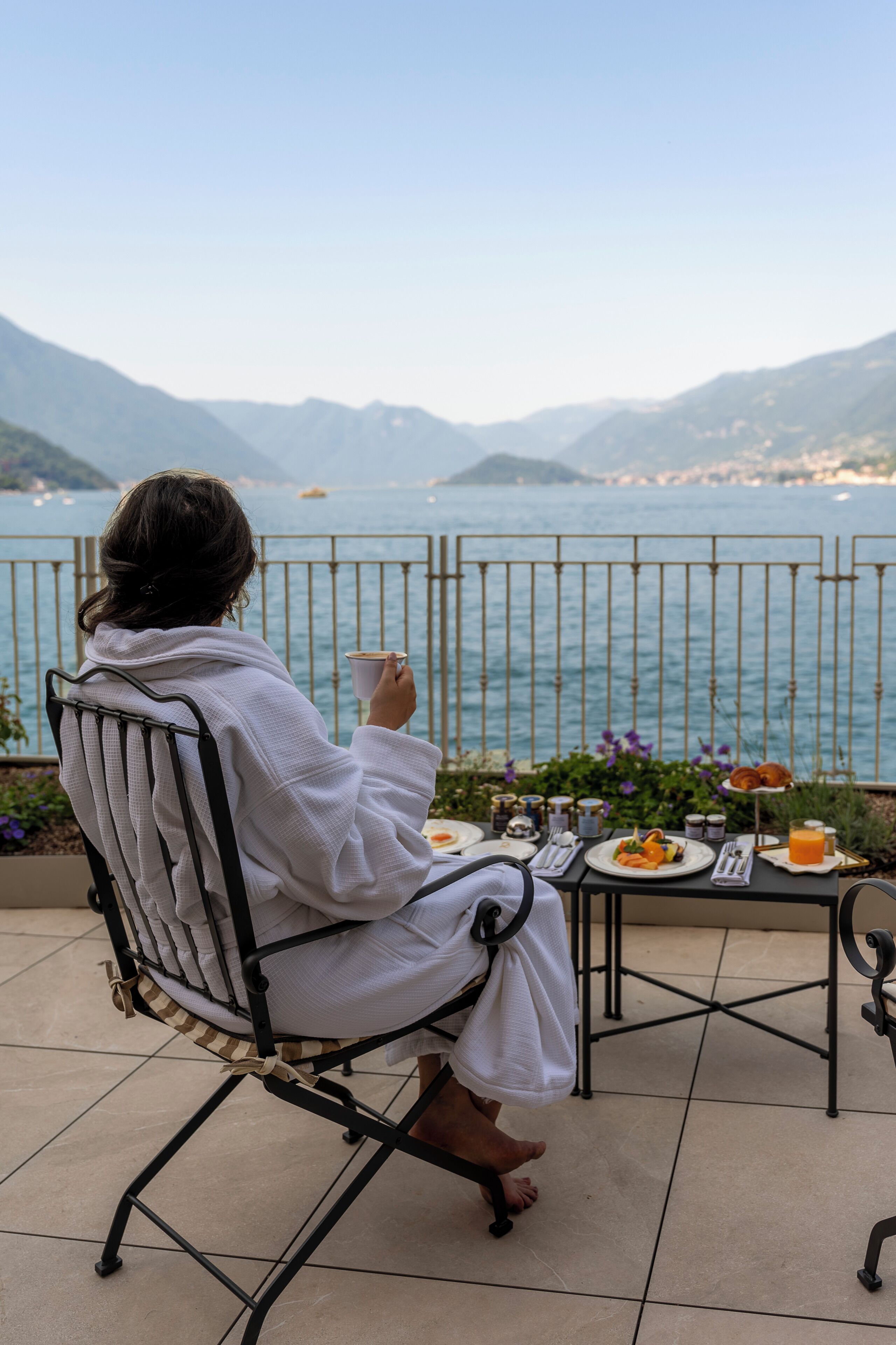 A person seated at a table with a view of the sea and mountains.