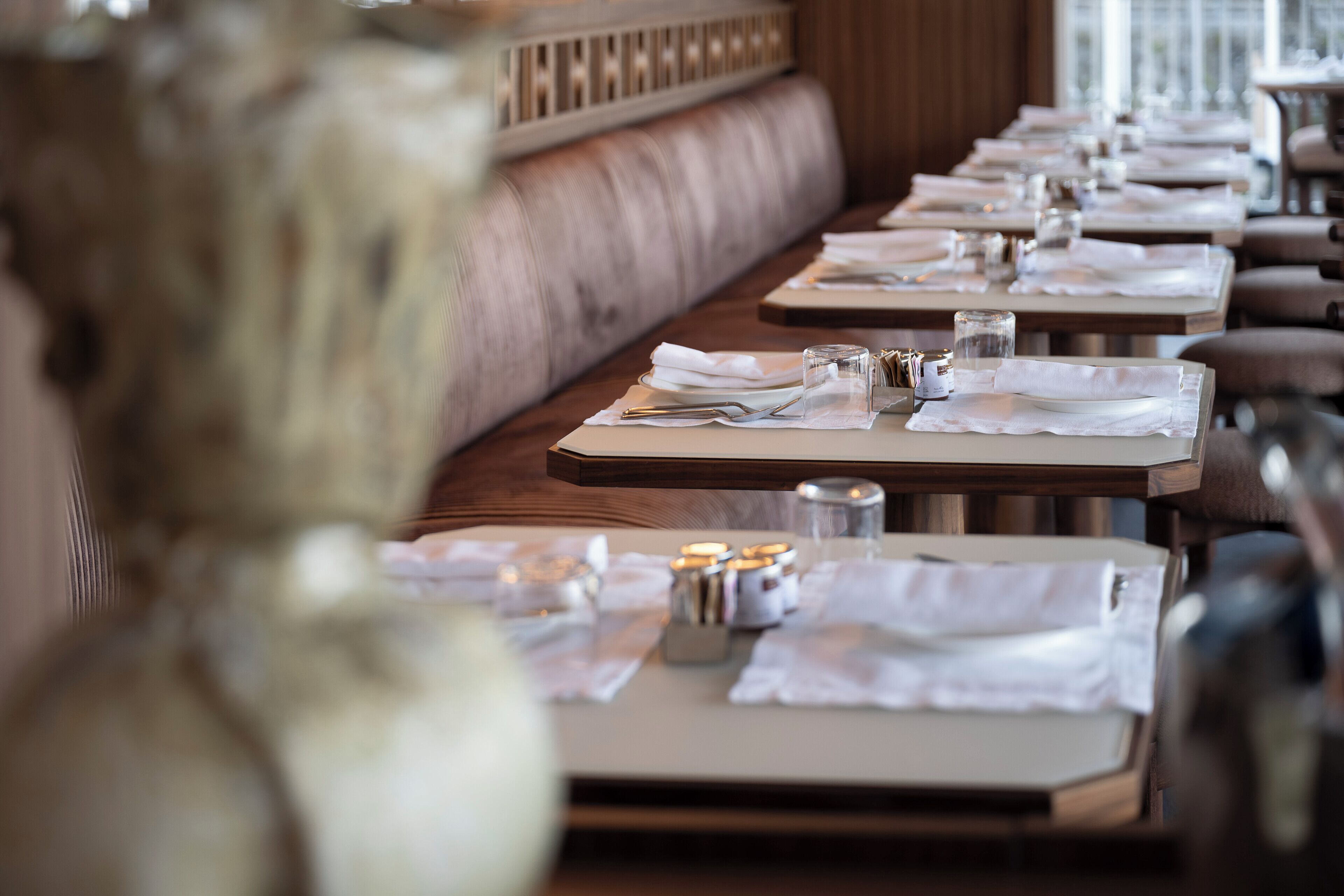 Un restaurant doté d’un long banc en bois servant de banquette, de tables recouvertes de nappes blanches et décorées de bougies.
