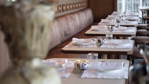 A restaurant with a long, wooden bench seating area, tables set with white tablecloths, and candles on the tables. - Palazzo Genazzini (Bellagio)