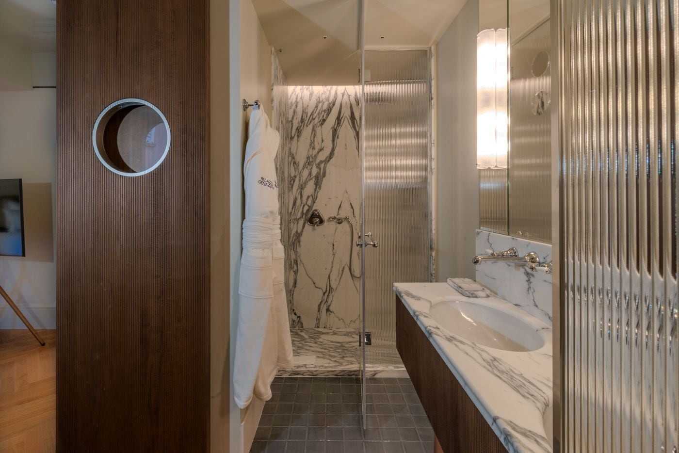 Un baño moderno con cabina de ducha de vidrio, encimeras de mármol y un panel de madera decorativo.