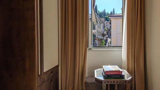 A room with a window, curtains, a radiator, and a stack of books on a small table. - Palazzo Genazzini (Bellagio)