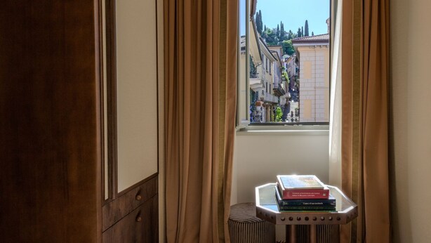 A room with a window, curtains, a radiator, and a small table with books. - Palazzo Genazzini (Bellagio)