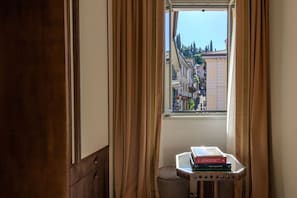 A room with a window, curtains, a radiator, and a small table with books. - Palazzo Genazzini (Bellagio)