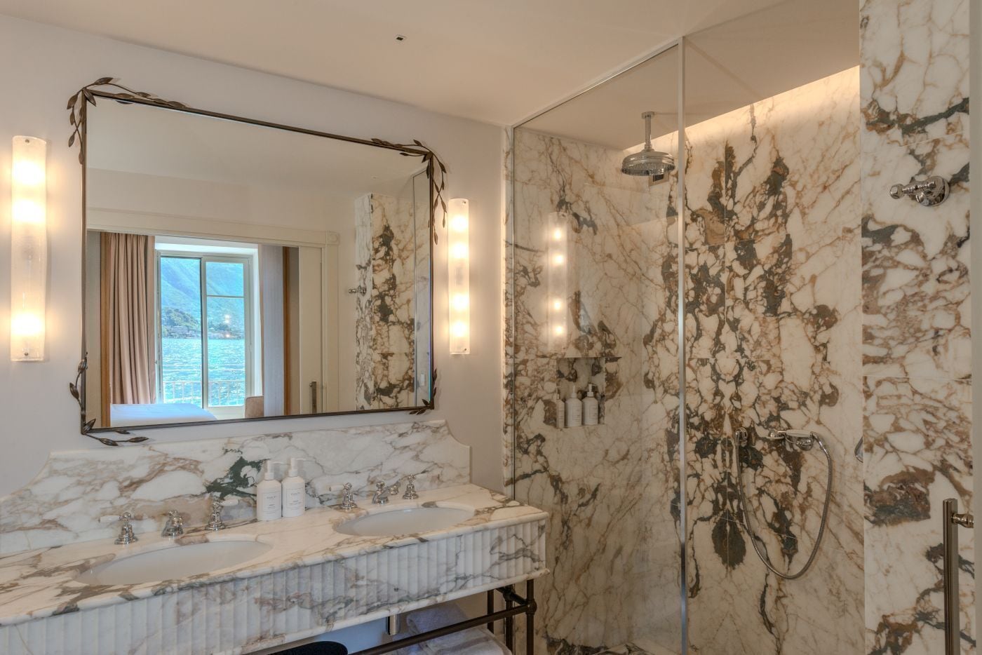 Une salle de bain avec un meuble-lavabo en marbre, un grand miroir et une cabine de douche en verre.