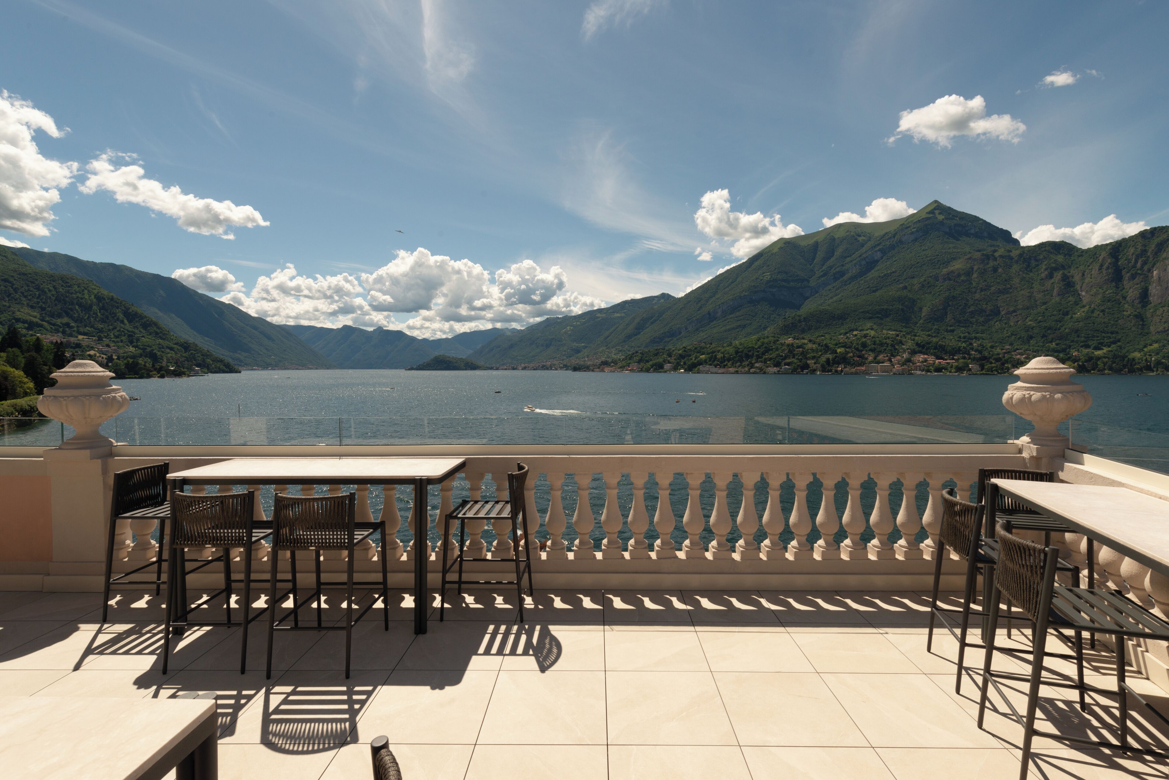 A terrace with a table and chairs overlooking a lake with mountains in the background.
