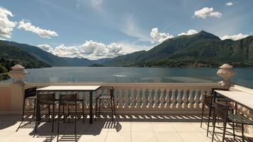 A terrace with a table and chairs overlooking a lake with mountains in the background.