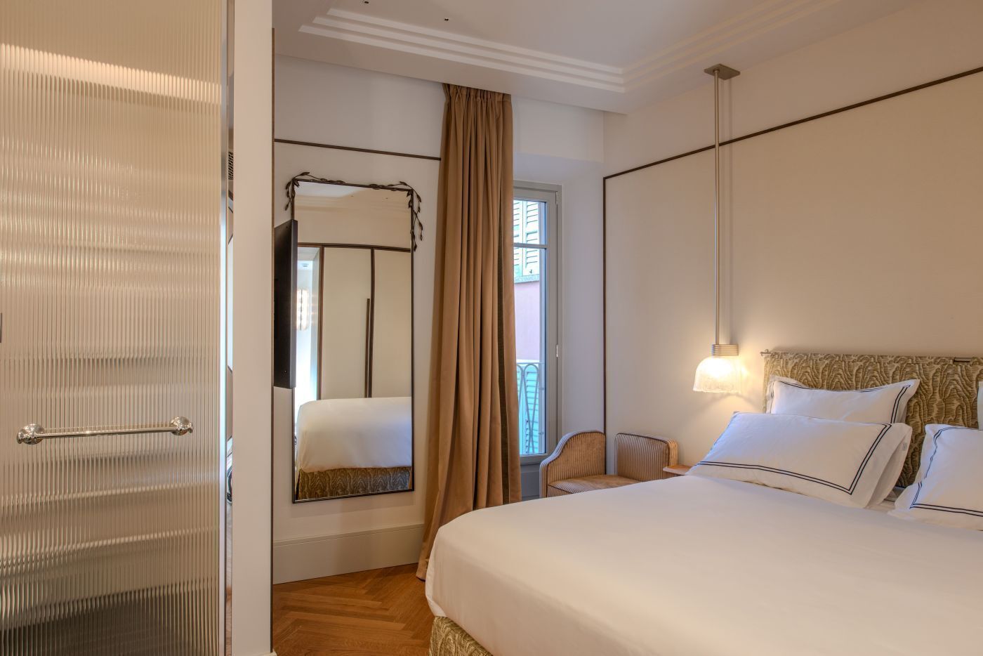 A hotel room with a large bed, a bedside table, a chair, a mirror, and a window with curtains.