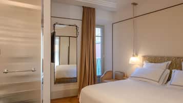 A hotel room with a large bed, a bedside table, a chair, a mirror, and a window with curtains.
