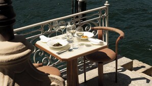 A dining table with plates, glasses, and cutlery, set against a railing overlooking water. - Palazzo Genazzini (Bellagio)
