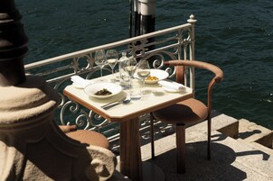 Una mesa de comedor con platos, vasos y cubiertos, frente a una barandilla con vista al agua.