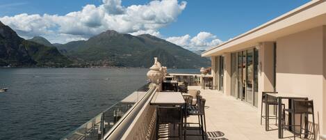 A terrace with tables and chairs overlooking a body of water and mountains.