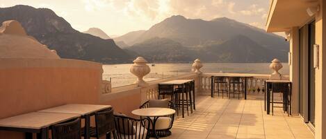 Eine Terrasse mit Tischen und Stühlen mit Blick auf ein Gewässer und Berge.