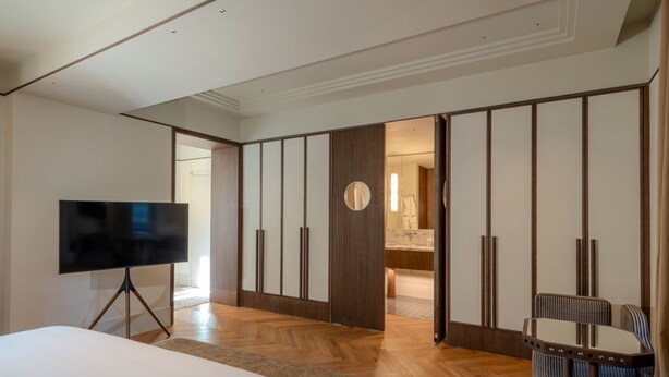 A hotel room with a bed, a TV on a stand, a wooden floor, a mirror, and a bathroom visible through an open door. - Palazzo Genazzini (Bellagio)