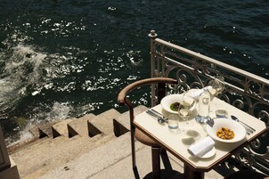 A table set with dinnerware, glasses, and a bowl of food, overlooking a body of water.