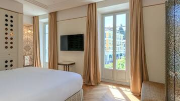 Ein Hotelzimmer mit einem großen Bett, einem an der Wand befestigten Fernseher, einem kleinen Tisch und Blick auf Gebäude durch das Fenster.