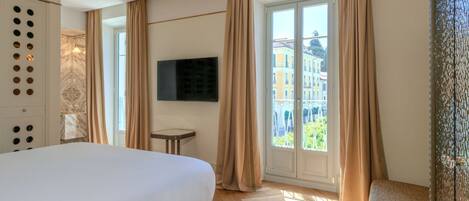 Habitación de hotel con una cama grande, un televisor en la pared, una mesita y vistas a edificios a través de la ventana.