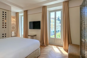 Une chambre d’hôtel avec un grand lit, un téléviseur fixé au mur, une petite table et une vue sur les bâtiments par la fenêtre.