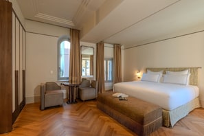 A hotel room with a large bed, two armchairs, a small table, and a wardrobe.