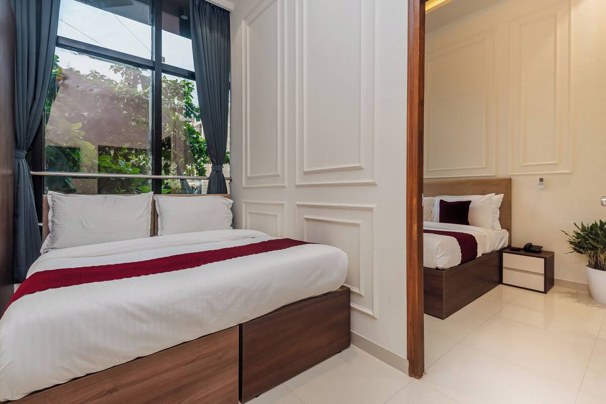 Un lit double agrémenté d’une touche de rouge, une table de chevet, un miroir et une plante en pot.