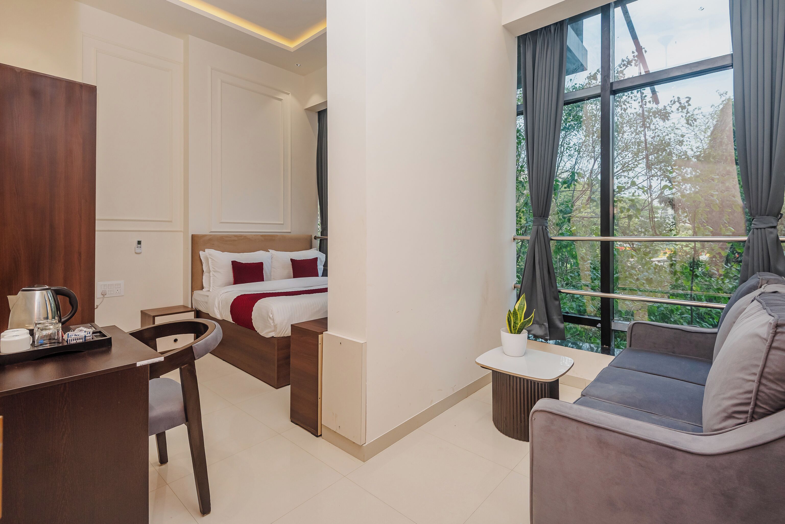 Ein modernes Hotelzimmer mit Bett, Sofa, Schreibtisch und einem großen Fenster mit Blick auf Grünflächen.