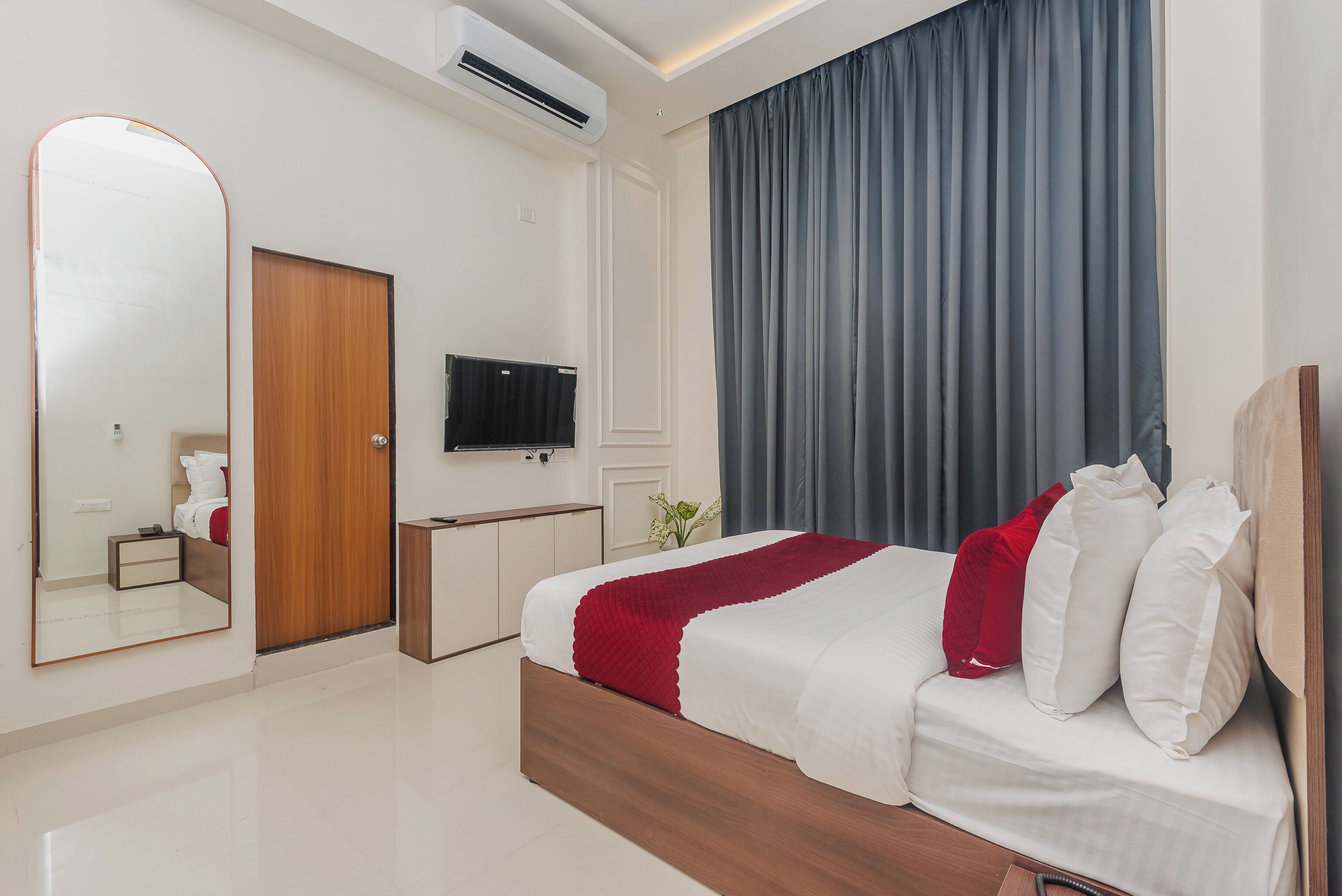 Une chambre d’hôtel moderne dotée d’un grand lit, d’un téléviseur à écran plat, d’une armoire en bois et d’un grand miroir.