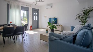 A modern living room with a sofa, a dining area with chairs, a TV, and a plant. - Sweet Sissi 2BR Residence with Jacuzzi Sleeps 6 (Sisi)