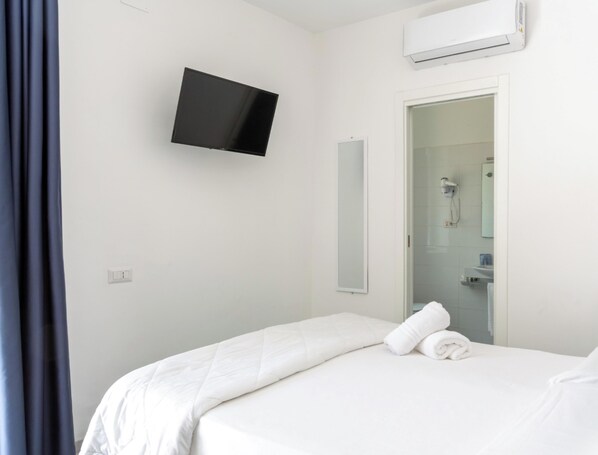 A hotel room with a bed, a flat-screen TV mounted on the wall, a shower area, and an air conditioning unit. - Hotiday Vico Equense Beach (Vico Equense)