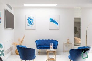 A modern room with a blue sofa, two chairs, a small round table with a vase, and two abstract paintings on the wall. - Hotiday Vico Equense Beach (Vico Equense)