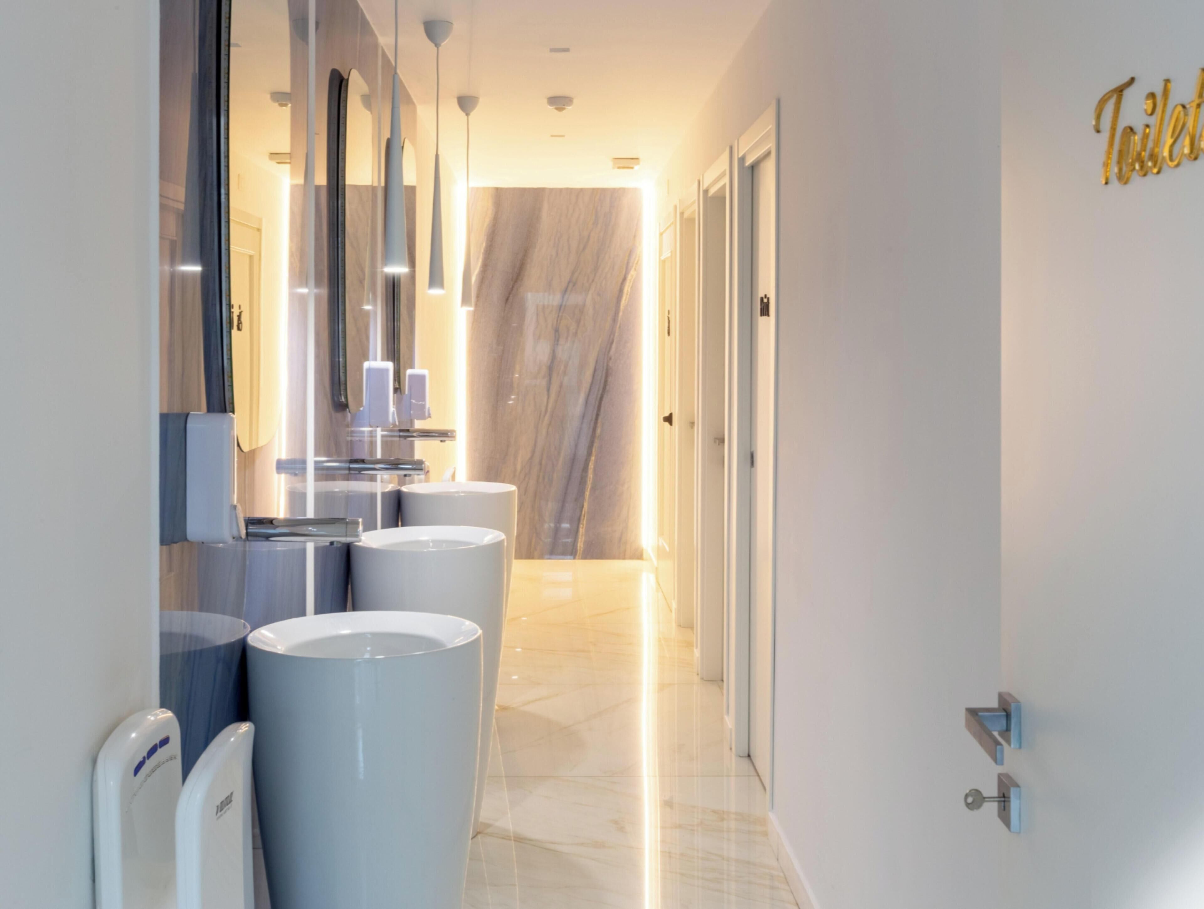 A modern bathroom with multiple sinks, a mirror, and a toilet.