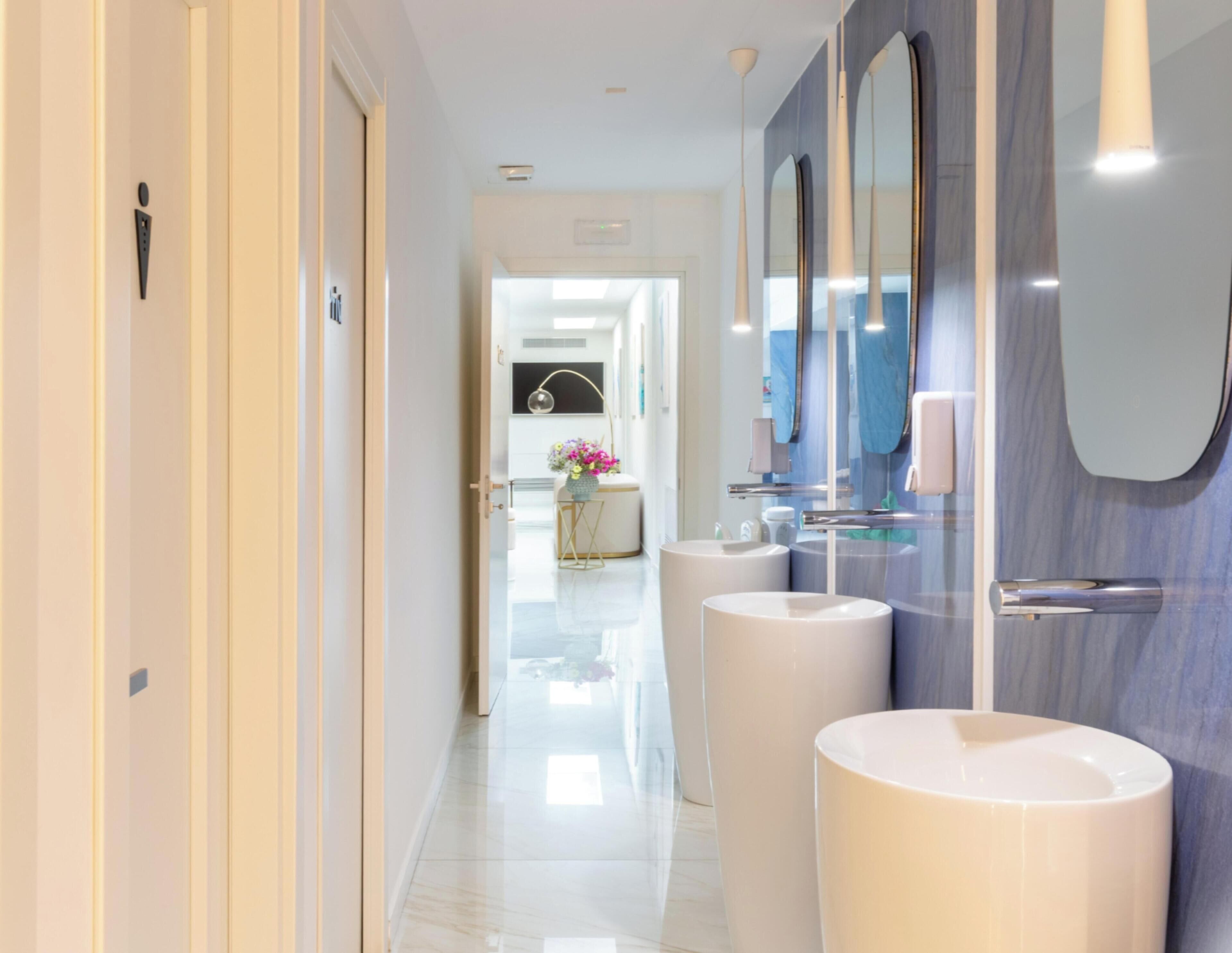A modern bathroom with two sinks, a mirror, and a door leading to another room.