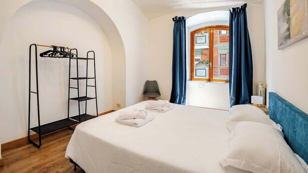 Hotellihuoneessa on sänky, musta metallinen vaatekaappi, tuoli ja ikkuna, jossa on siniset verhot.