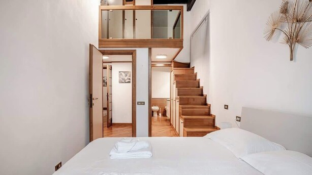 Quarto com uma cama grande, escada de madeira e vista para o banheiro.