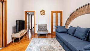 Uma sala de estar com um sofá azul, uma poltrona cinza, um banco de madeira e um tapete estampado.