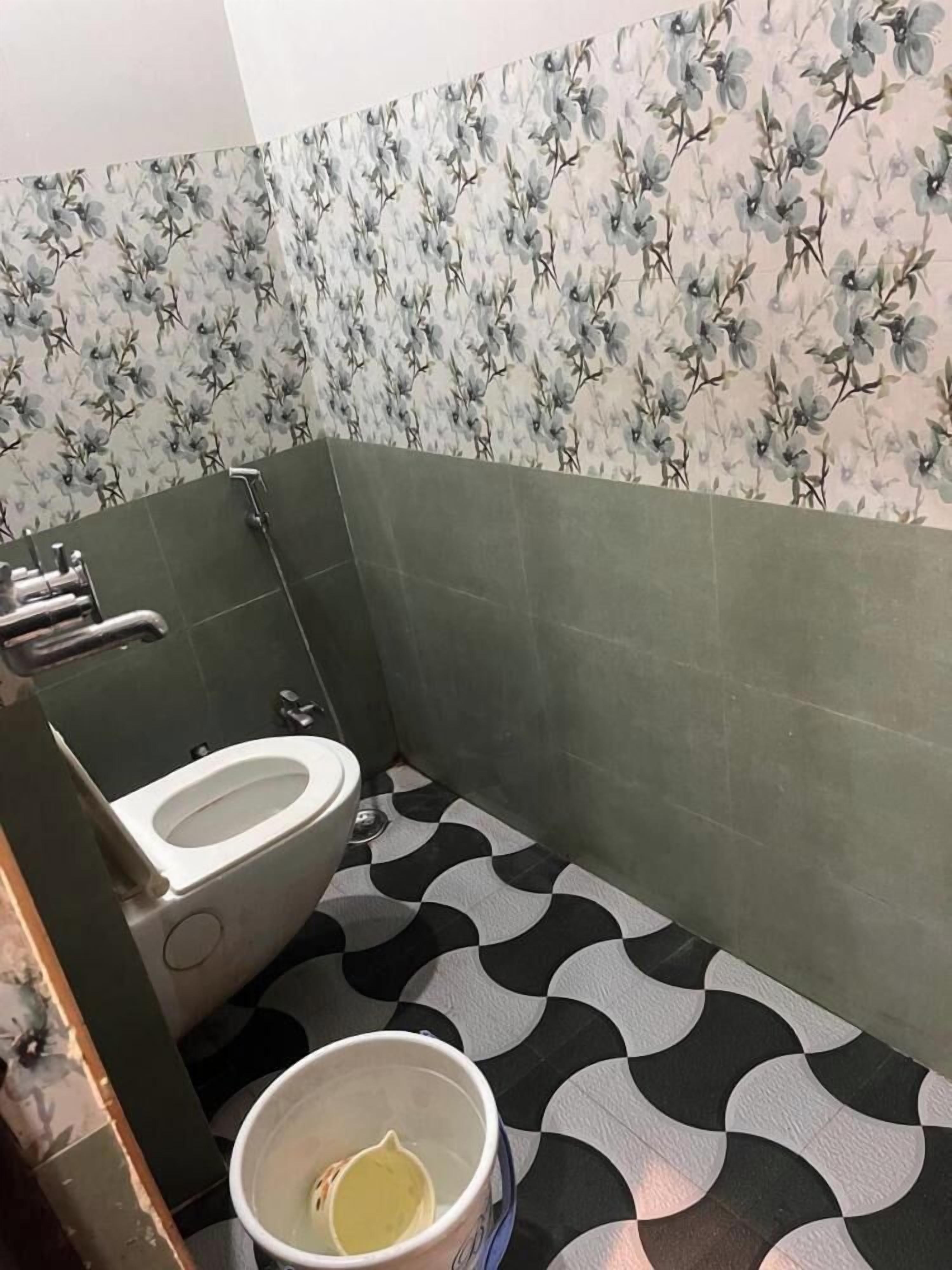 A bathroom with a toilet, a shower, and a bucket.