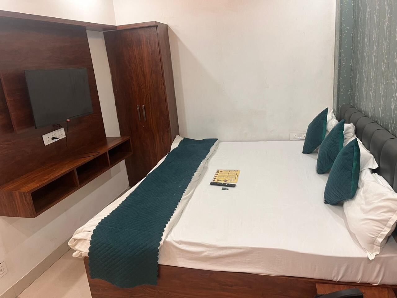 A bedroom with a bed, a TV mounted on the wall, and a wooden wardrobe.
