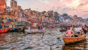 A river with boats and people, a temple with a spire, and buildings along the riverbank.