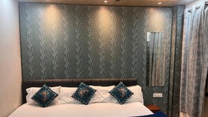 A neatly made bed with white linens and two decorative pillows, a dark headboard, and a wall with a tree pattern.