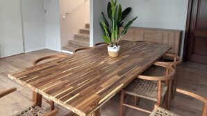 A dining area with a wooden table, woven chairs, a staircase, and a potted plant. - Luga Homes - Augustusplatz (Leipzig)