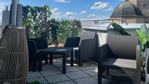 An outdoor seating area with wicker furniture, a large vase, and potted plants. - Luga Homes - Augustusplatz (Leipzig)